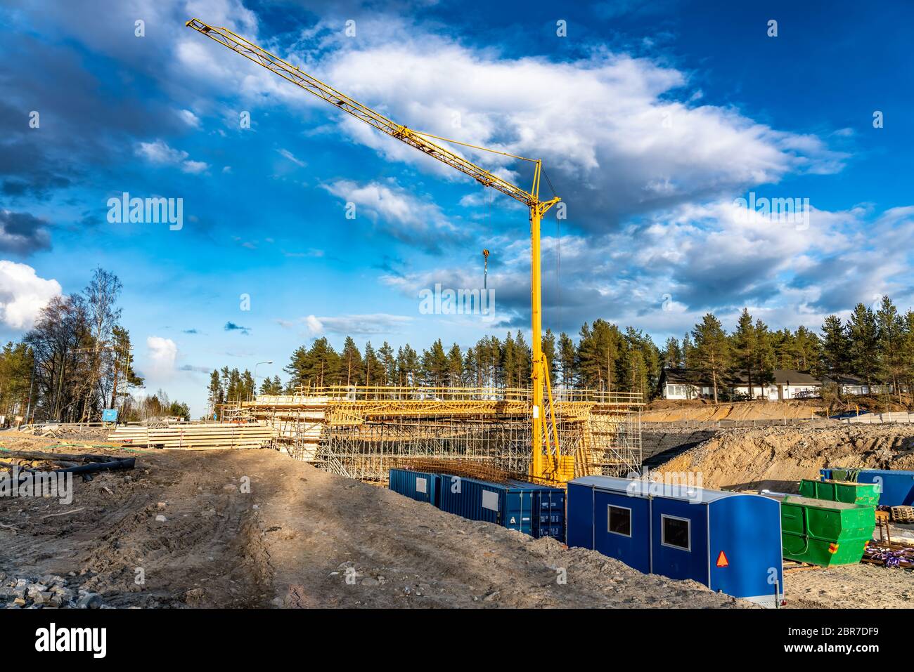 Foto von neuer Brückenbaustelle mit Holzbauweise zur weiteren Befüllung mit Beton. Gelber Kranturm, blaue Wolken, tiefer Graben. Stockfoto