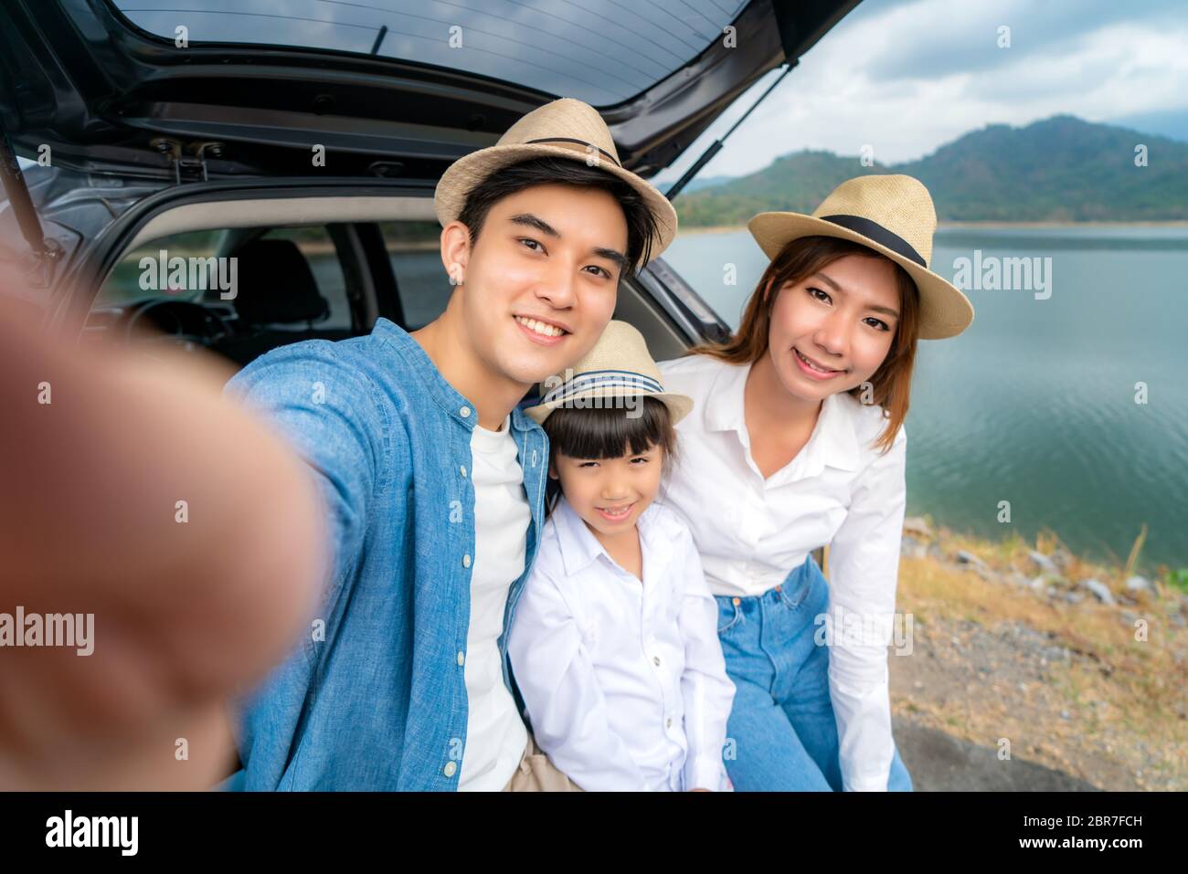Porträt der asiatischen Familie, die mit Vater, Mutter und Tochter selfie im Auto sitzt, mit See- und Bergblick, mit Smrtphone während des gemeinsamen Urlaubs in ho Stockfoto