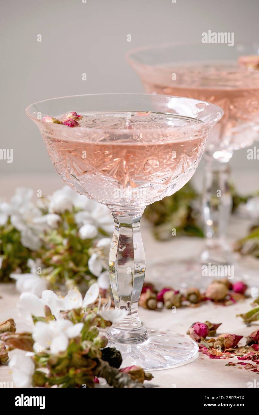 Kristallgläser aus rosa Rosenchampagner, Apfelwein oder Limonade mit trockenen Rosenblüten. Blüte Kirsche Zweige oben. Hintergrund aus rosa Marmor Stockfoto