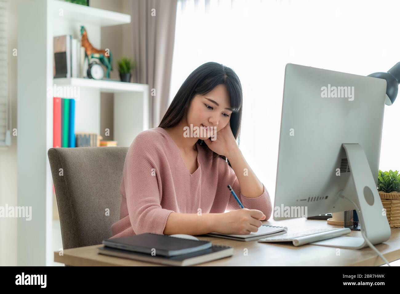 Junge asiatische Geschäftsfrau, die Computerarbeit von zu Hause aus zum Schutz von Viren verwendet und sich um ihre Gesundheit von COVID-19 kümmert. Arbeiten zu Hause und Sozialdist Stockfoto