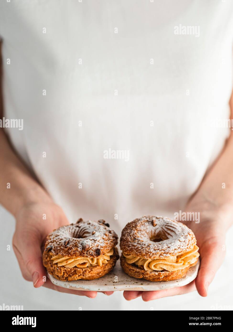 Frau in weißem T-Shirt hält Teller mit zwei Choux Paris Brest Gebäck mit Haselnuss Stockfoto