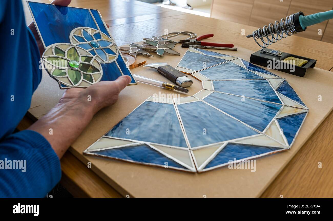 Frau, die an Hobby-Handwerk Buntglasscheiben mit Werkzeugen arbeitet, Schottland, Großbritannien Stockfoto