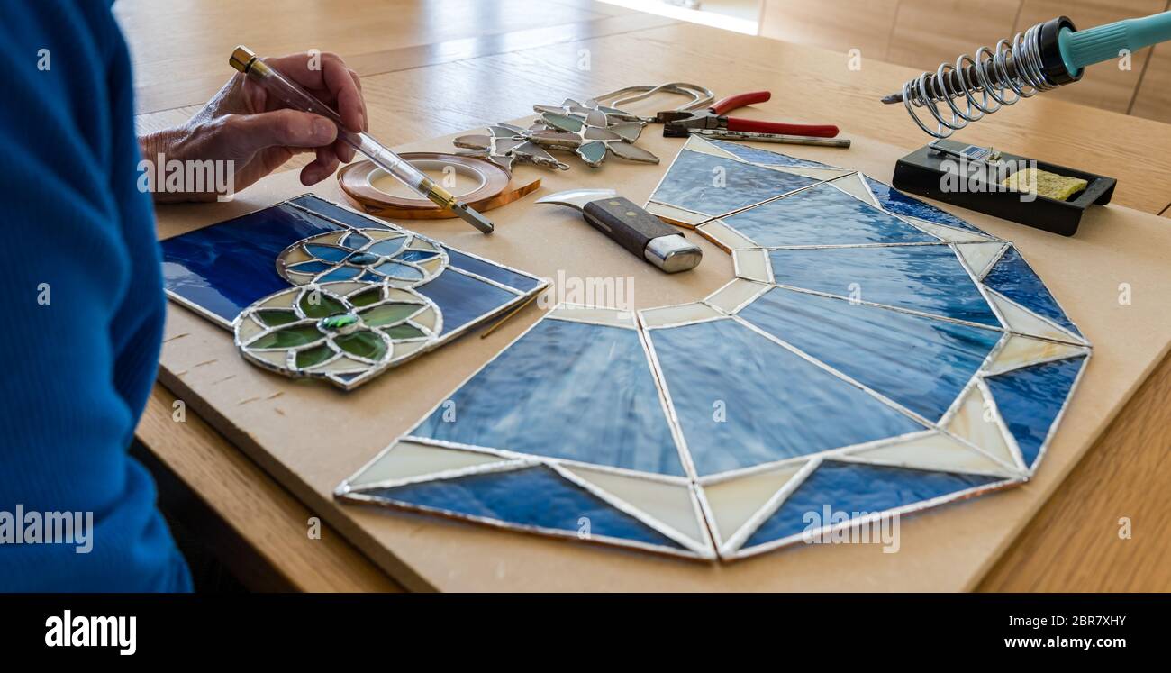 Frau, die an Hobby-Handwerk Buntglasscheiben mit Werkzeugen arbeitet, Schottland, Großbritannien Stockfoto