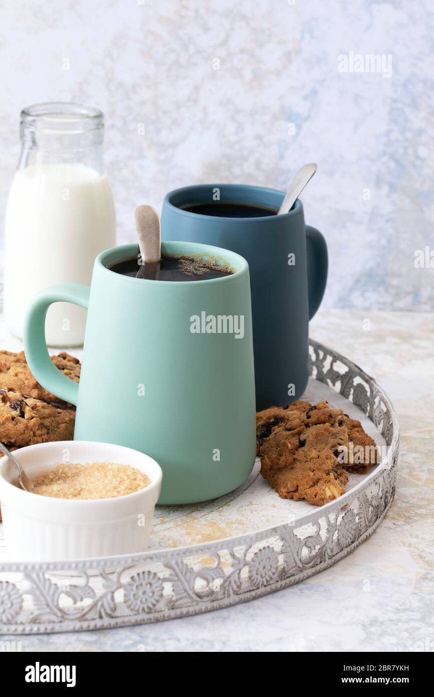 Tassen schwarzen Kaffee auf einem Serviertablett mit Milch, Zucker und Sultaninen-Cookies. Stockfoto