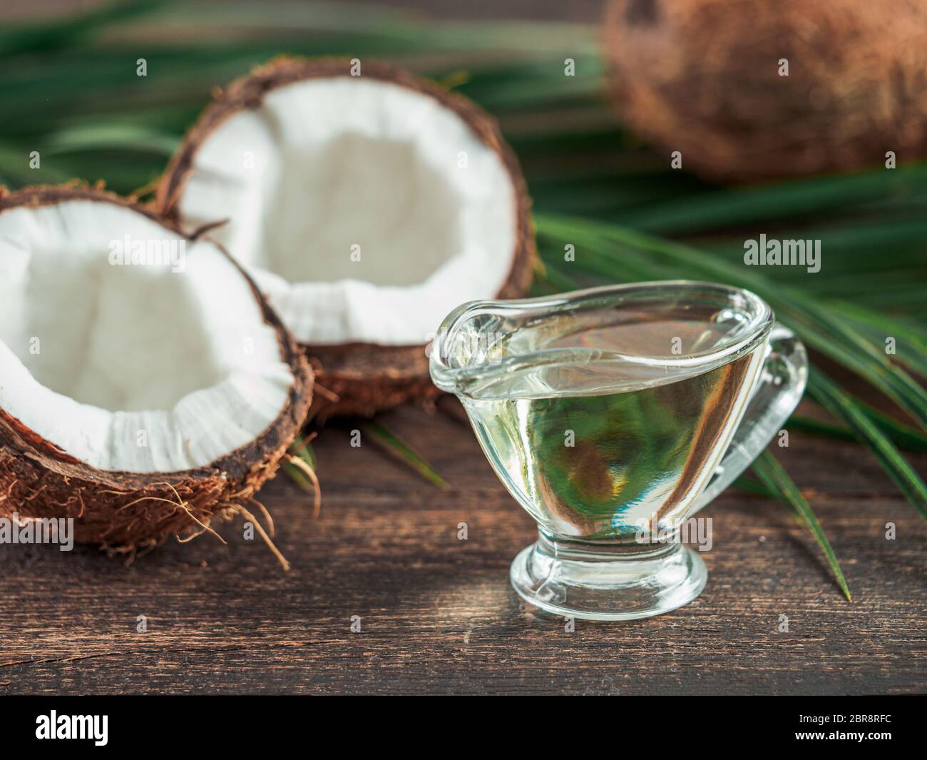 Flüssiges Kokosöl MCT und halbierte Kokosnuss auf Holztisch. Gesundheitliche Vorteile von MCT-Öl. MCT oder mittelkettige Triglyceride, Form von gesättigten Fettsäuren aci Stockfoto