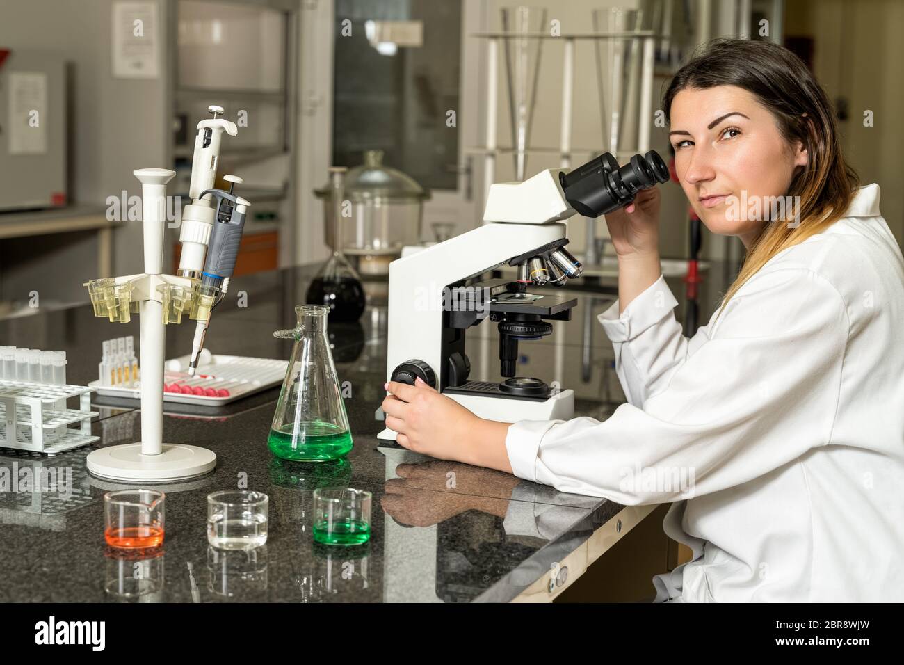 Mittleren Alters, Kaukasische weiß, weiblich Labortechniker in eine weiße Robe mit Stethoskop, Mikroskop, Laboratorium, in Verbindung, Gerät ein Stockfoto