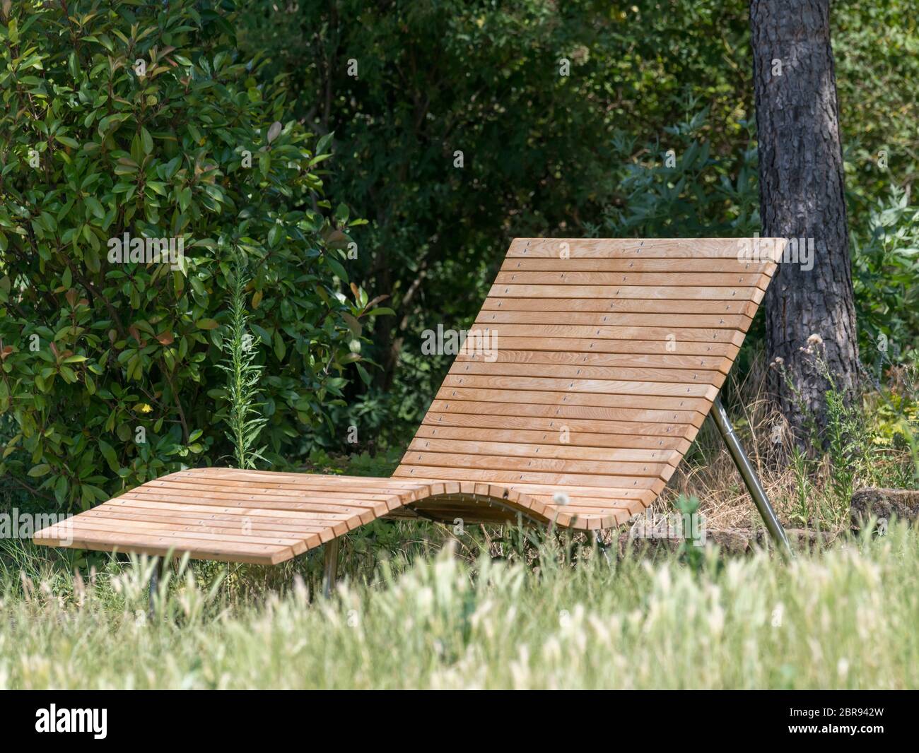 Holz- Liege auf einer Wiese vor grünem Hintergrund in der Sonne Stockfoto