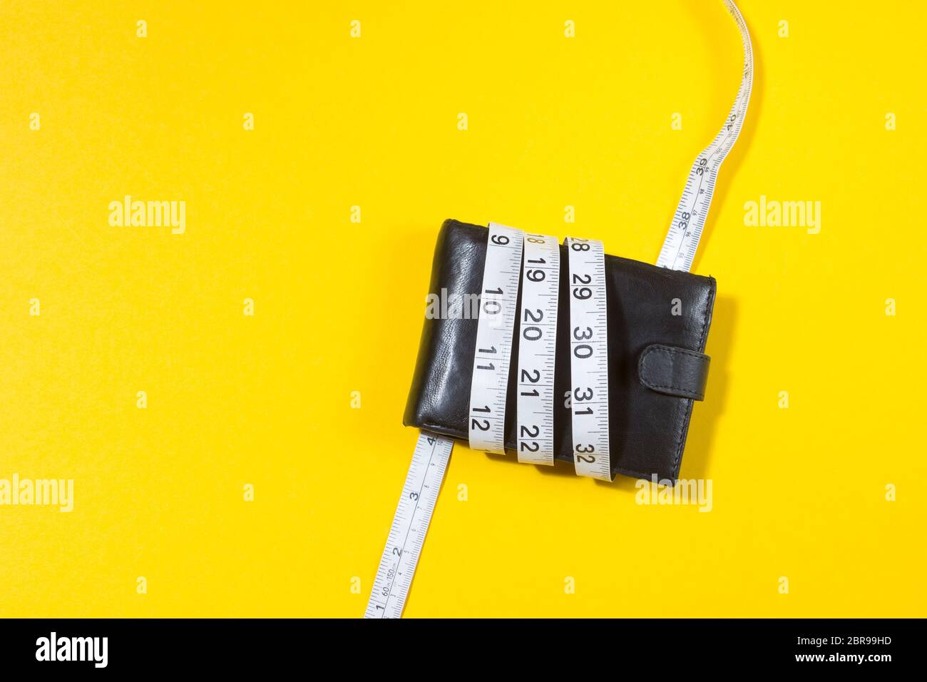 Konzept der Haushaltsplan und Geld. Geldbeutel ist mit Maßband auf gelbem Hintergrund gebunden Stockfoto