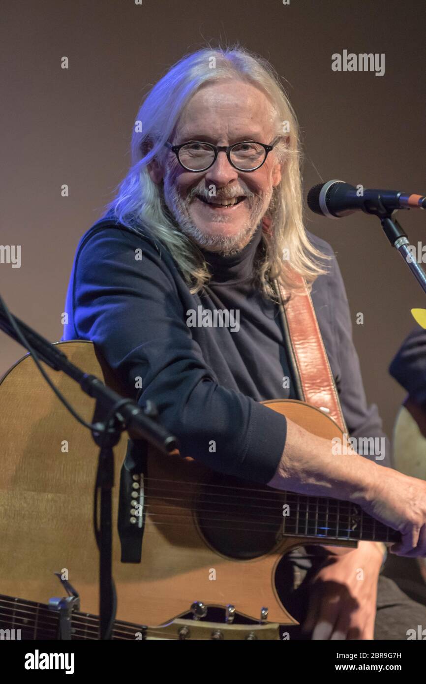 Musicain, mit langen weißen Haaren, lachend, während sie mit der Menge plaudern. Singen und spielen akustische Gitarre Stockfoto