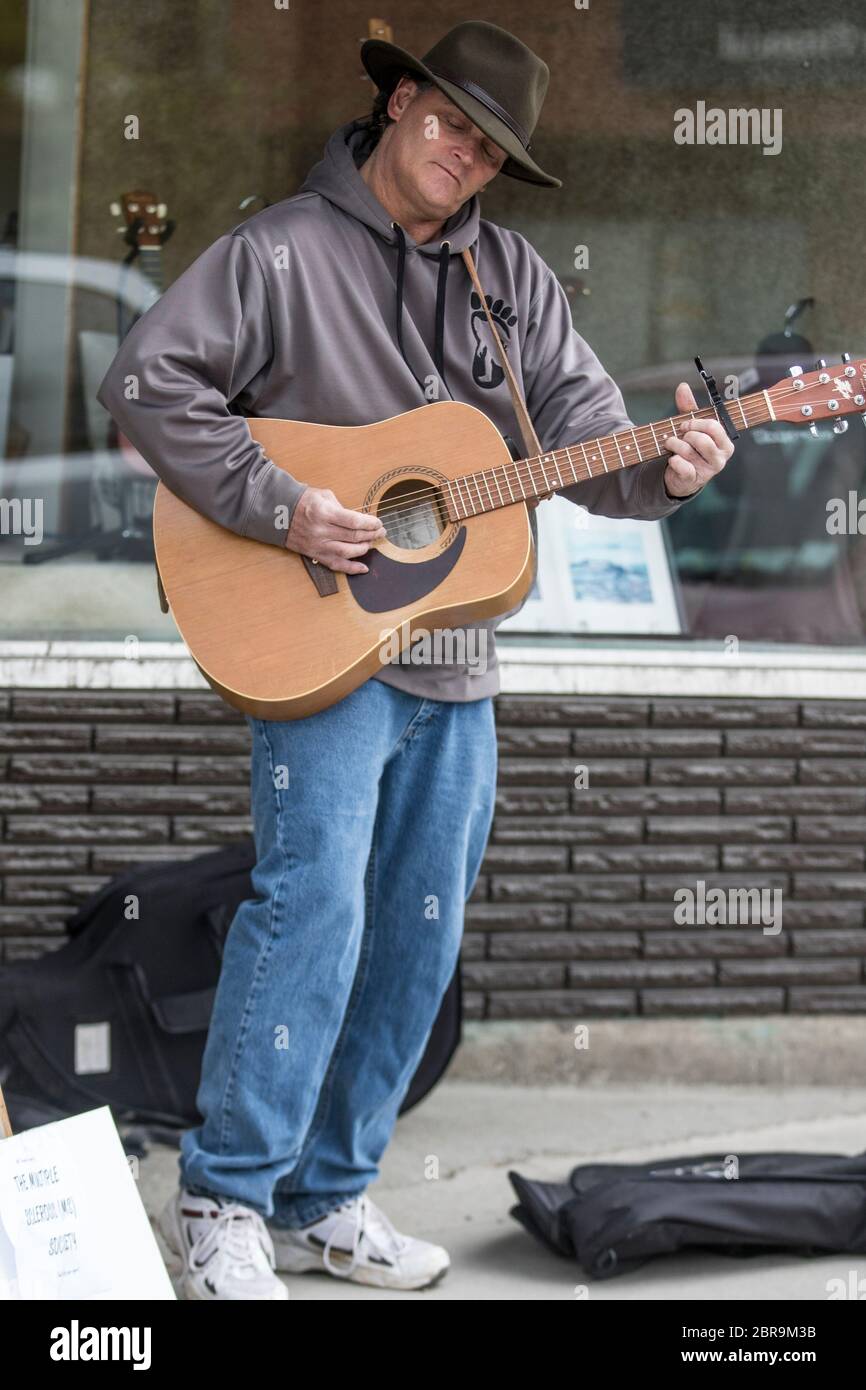 Cowboy-Sänger, Akustikgitarre spielend, auf der Straße unterwegs, an einem sonnigen Tag. Stockfoto