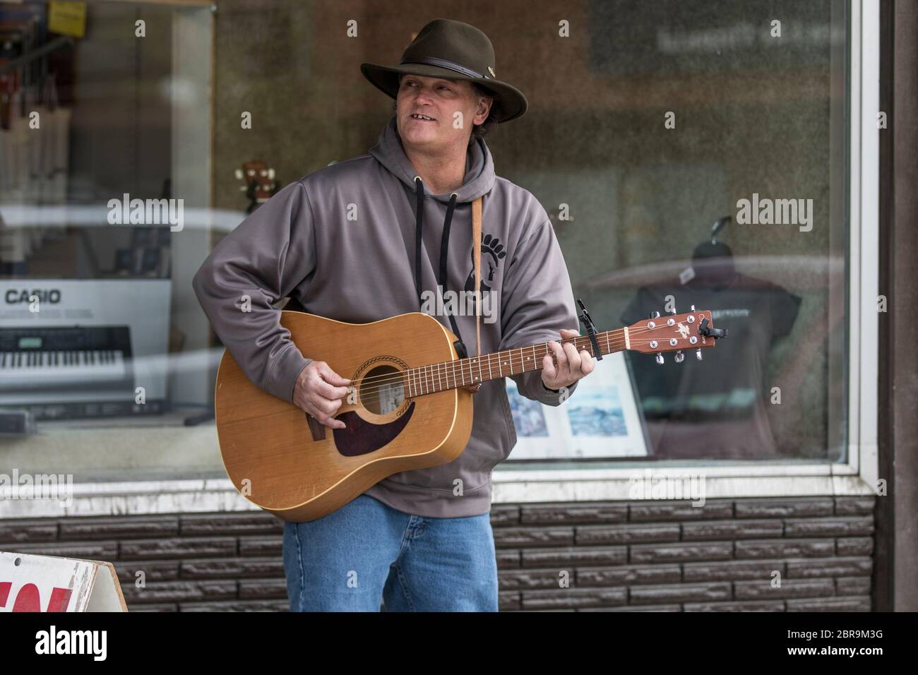 Cowboy-Sänger, Akustikgitarre spielend, auf der Straße unterwegs, an einem sonnigen Tag. Stockfoto