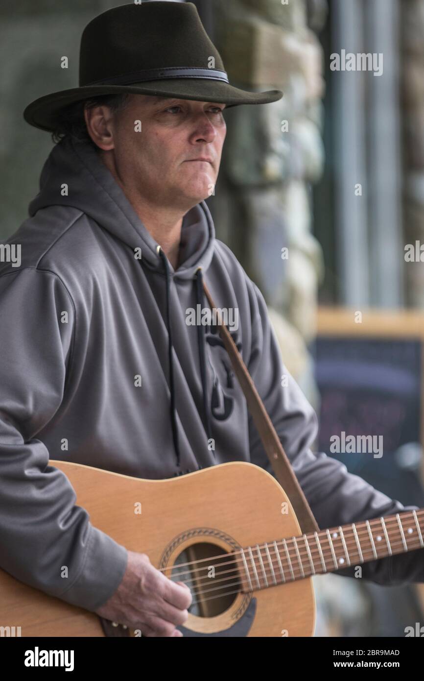 Cowboy-Sänger, Akustikgitarre spielend, auf der Straße unterwegs, an einem sonnigen Tag. Stockfoto