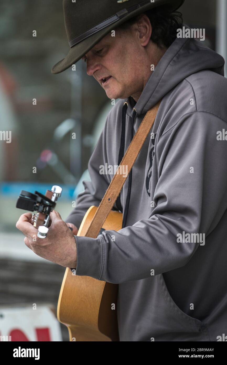 Cowboy-Sänger, Akustikgitarre spielend, auf der Straße unterwegs, an einem sonnigen Tag. Stockfoto