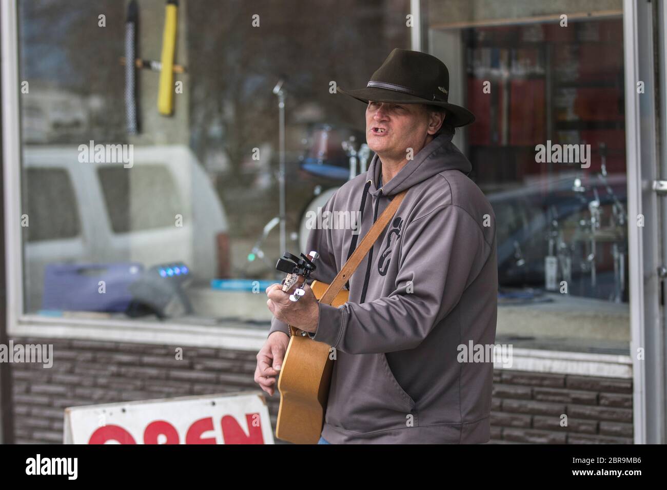 Cowboy-Sänger, Akustikgitarre spielend, auf der Straße unterwegs, an einem sonnigen Tag. Stockfoto