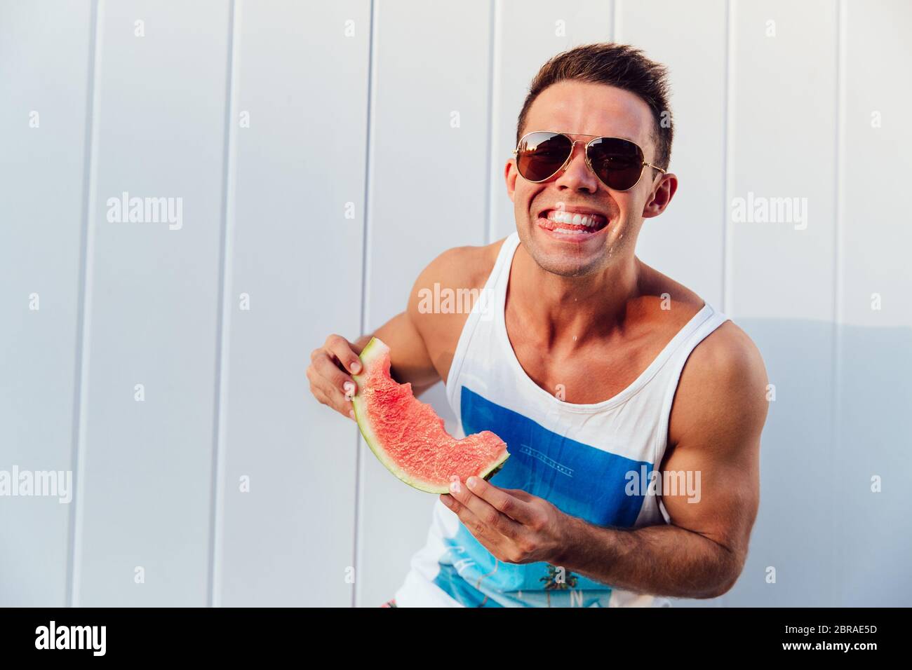 Sommer Foto von lächelnden sportlicher Mann mit Wassermelone, genießen, Essen, an der Kamera suchen, mit Sonnenbrille, im Freien. Stockfoto
