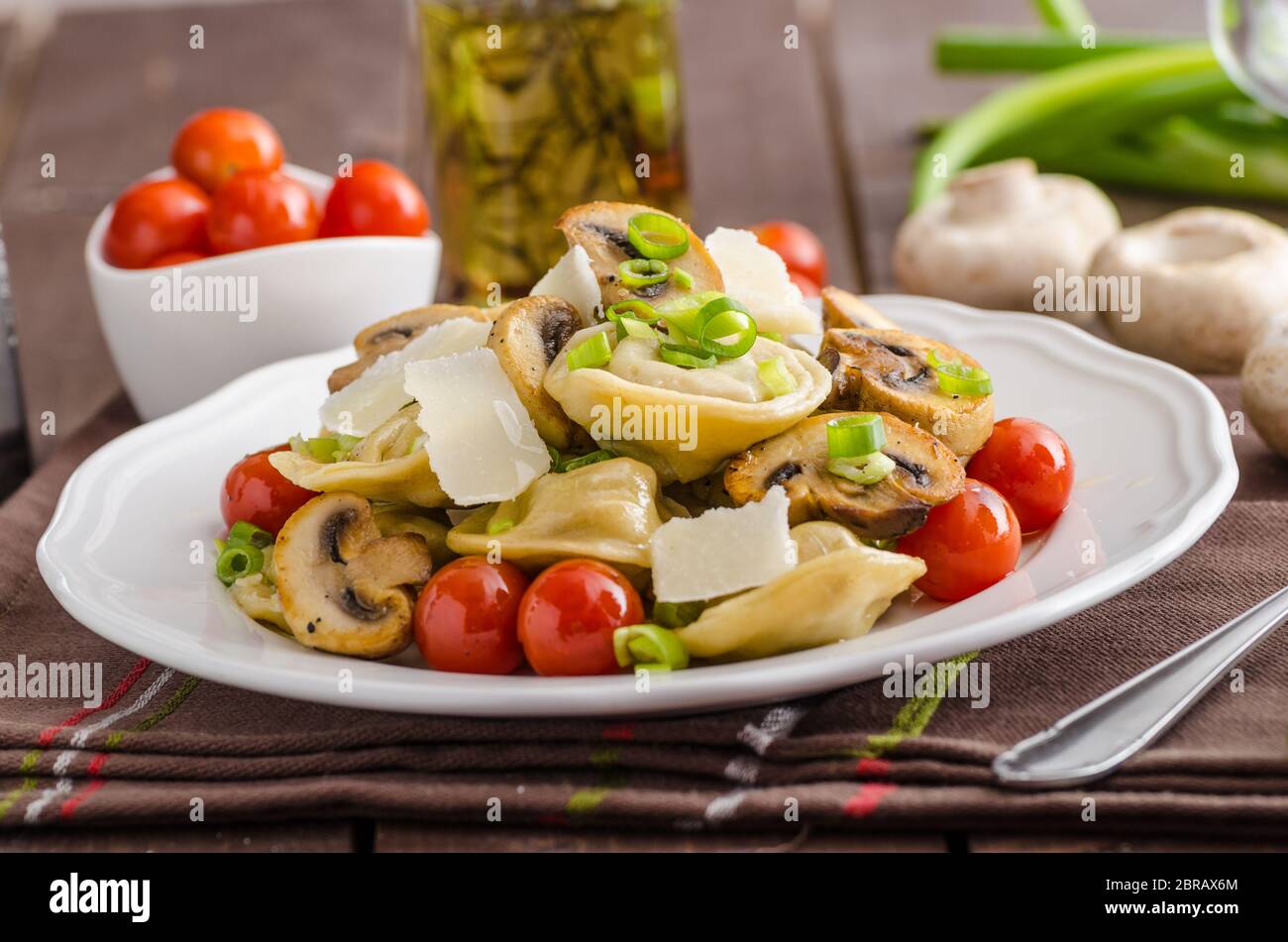 Hausgemachte Tortellini gefüllt mit Pilzen und Frühlingszwiebeln, gerösteten Tomaten, Knoblauch Souce gekrönt parmesan Stockfoto