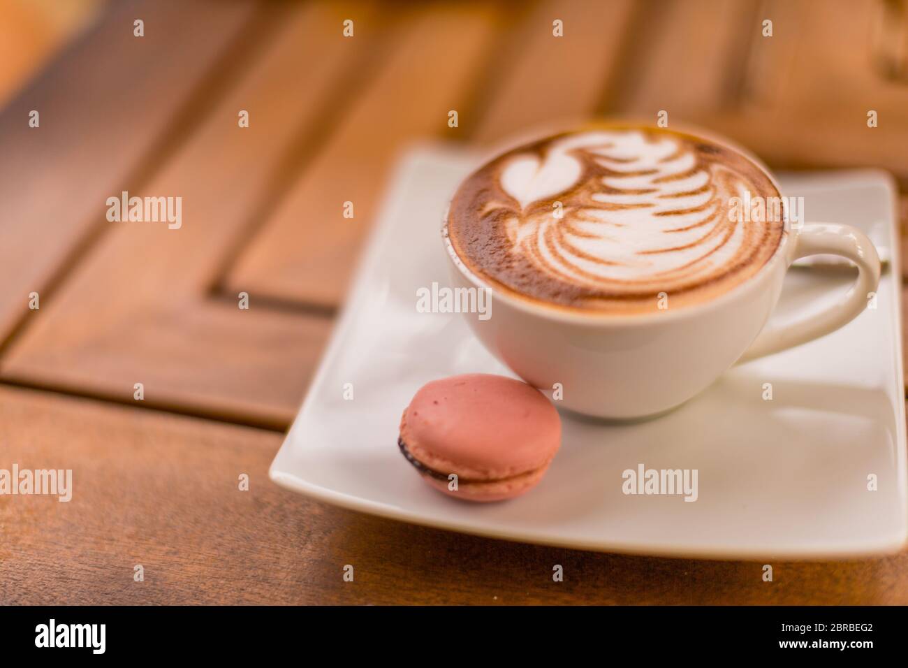 Nahaufnahme von heißem Cappuccino Latte Kaffee mit schönen Latte Art in einer weißen Keramik-Tasse auf einem Holztisch Hintergrund und Macaron Cookie Stockfoto