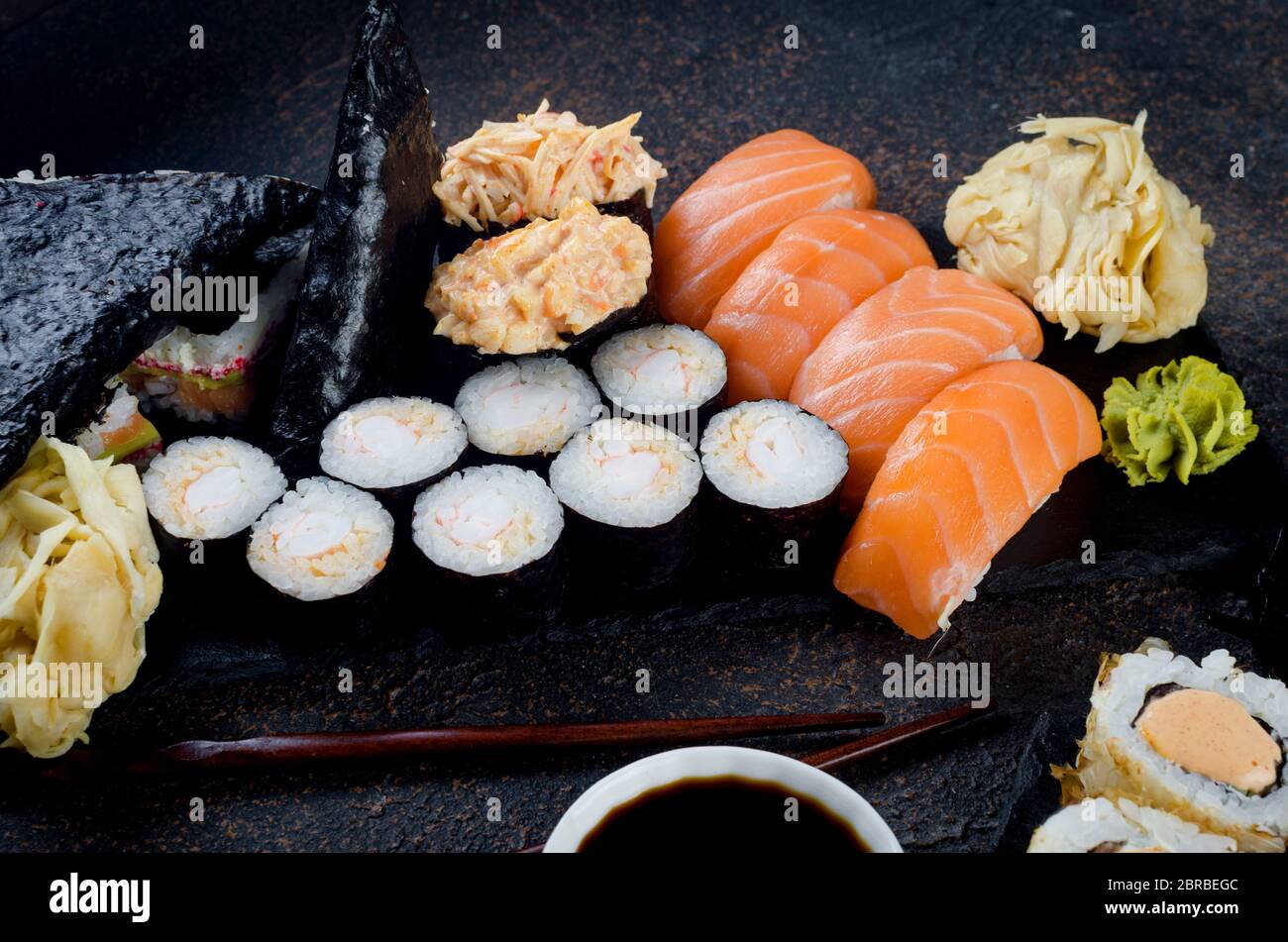 Leckere Sushi-Brötchen mit Soßen, Ingwer und Wasabi auf dunkel Stockfoto
