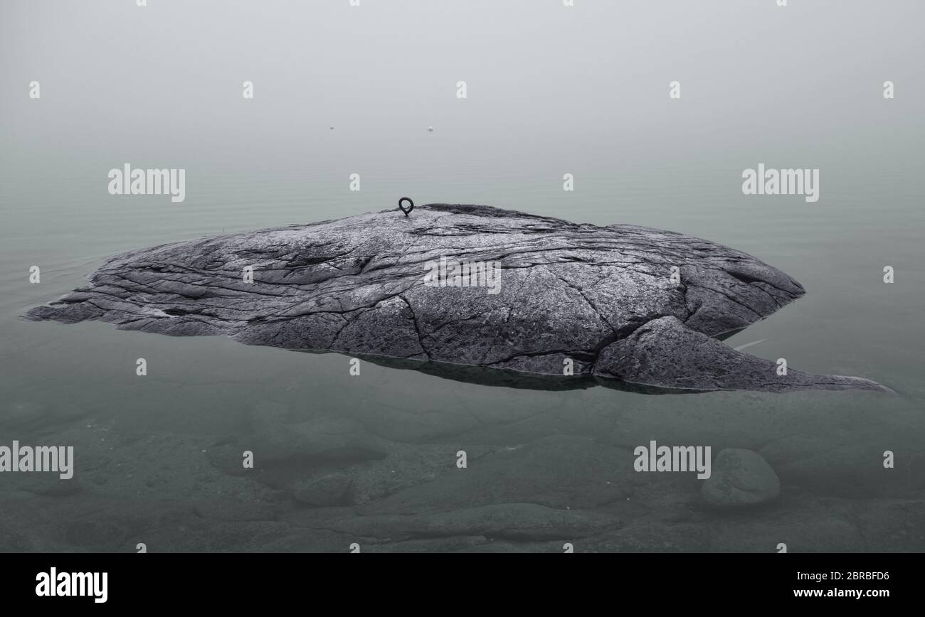 Kleine felsige Insel auf der Ostsee mit Boot Dock Leiste oben und paar Bojen auf dem Hintergrund im dichten Nebel im Anfang November Stockfoto