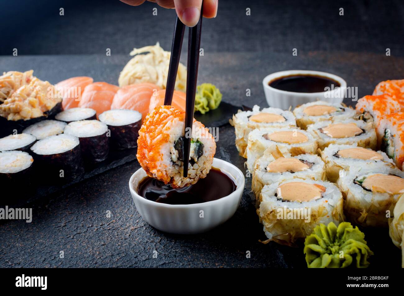Leckere Sushi-Brötchen mit Soßen, Ingwer und Wasabi auf dunkel Stockfoto