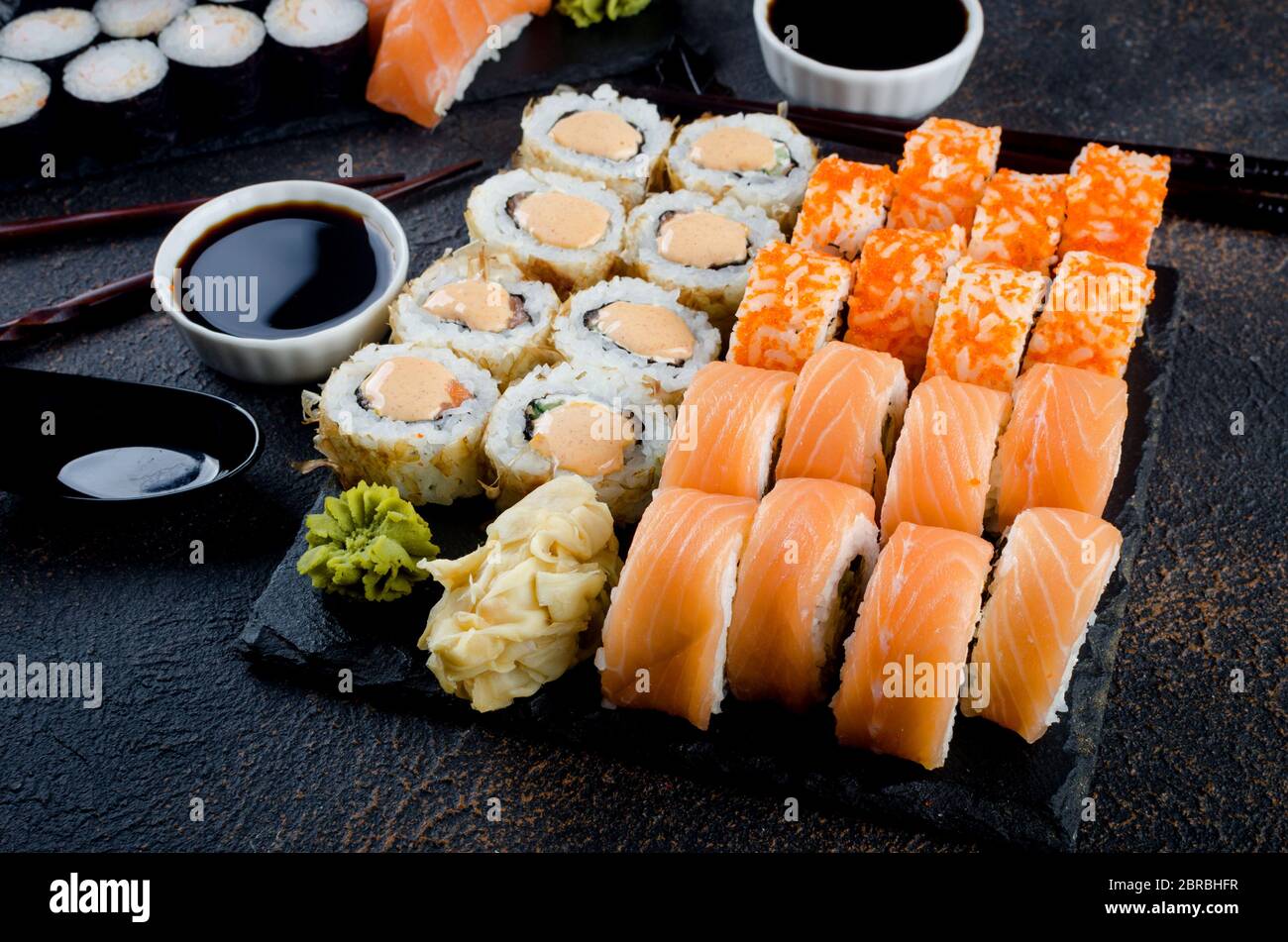 Leckere Sushi-Brötchen mit Soßen, Ingwer und Wasabi auf dunkel Stockfoto