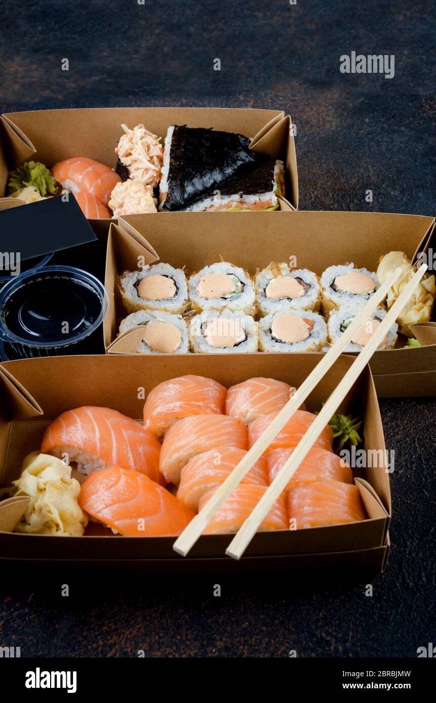 Leckere Sushi-Brötchen in Einweg-Kraftpapier-Boxen, Saucen, Essstäbchen. Sushi zum Mitnehmen oder Anliefern Stockfoto