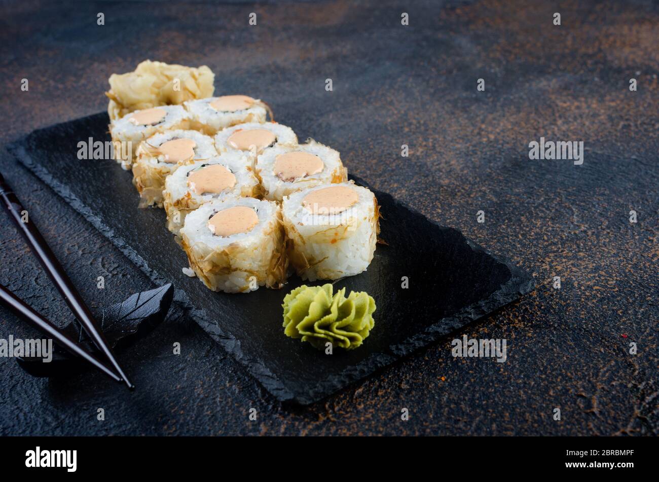 Sushi-Brötchen auf Steinplatte mit Saucen, Essstäbchen, Ingwer und Wasabi Stockfoto