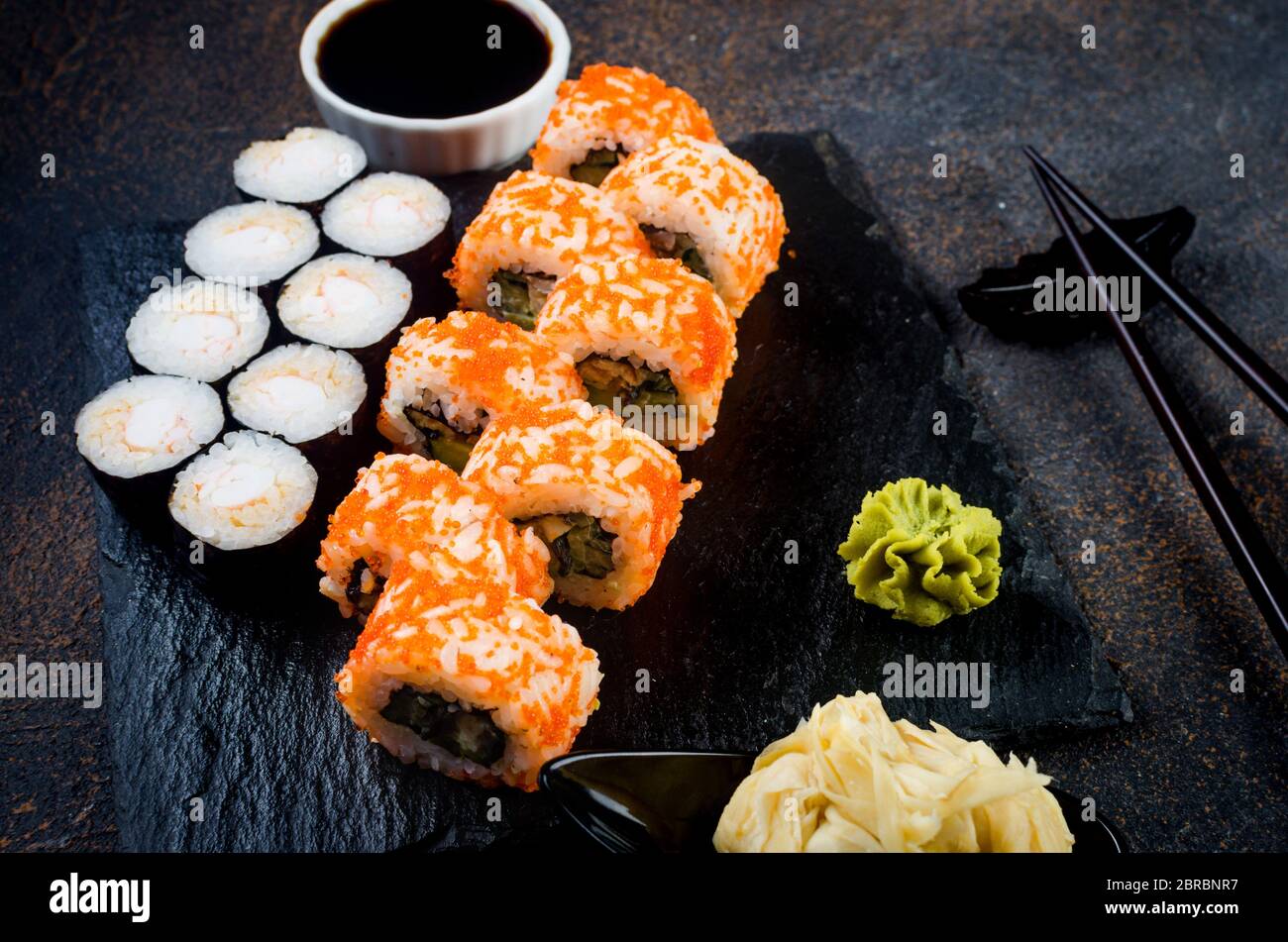 Maki-Brötchen auf Steinplatte mit Soßen, Ingwer und Wasabi Stockfoto
