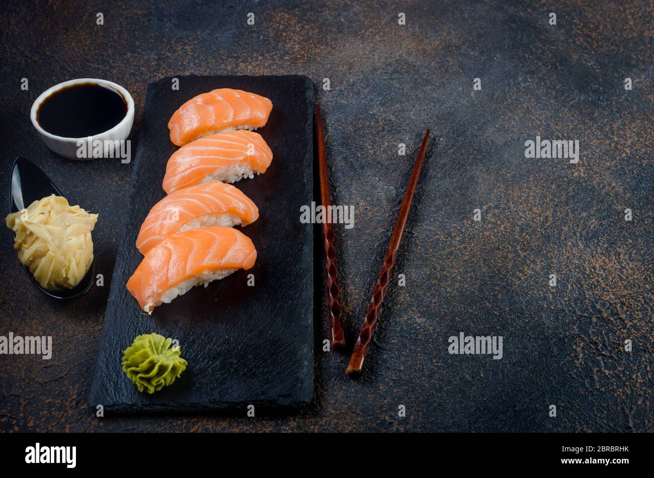 Leckeres Nigiri Sushi mit Lachs auf schwarzem Steinteller mit Sojasoße, Ingwer, Wasabi Stockfoto