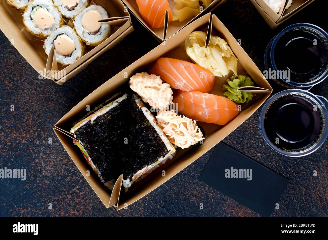 Leckere Sushi-Brötchen in Einweg-Kraftpapier-Boxen, Saucen, Essstäbchen. Sushi zum Mitnehmen oder Anliefern Stockfoto