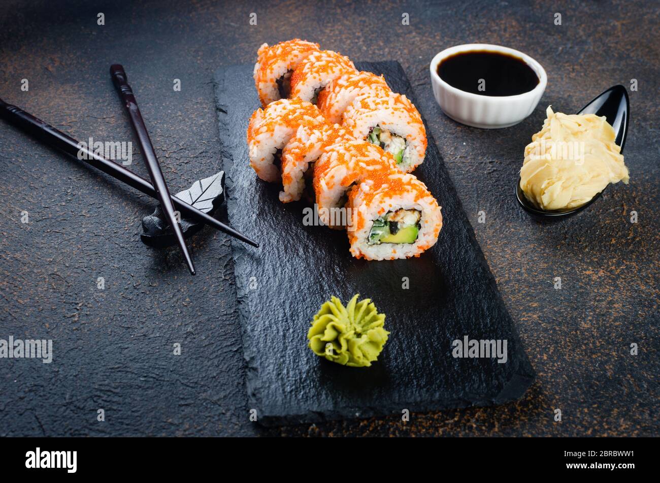 Sushi-Brötchen auf Steinplatte mit Saucen, Essstäbchen, Ingwer und Wasabi Stockfoto