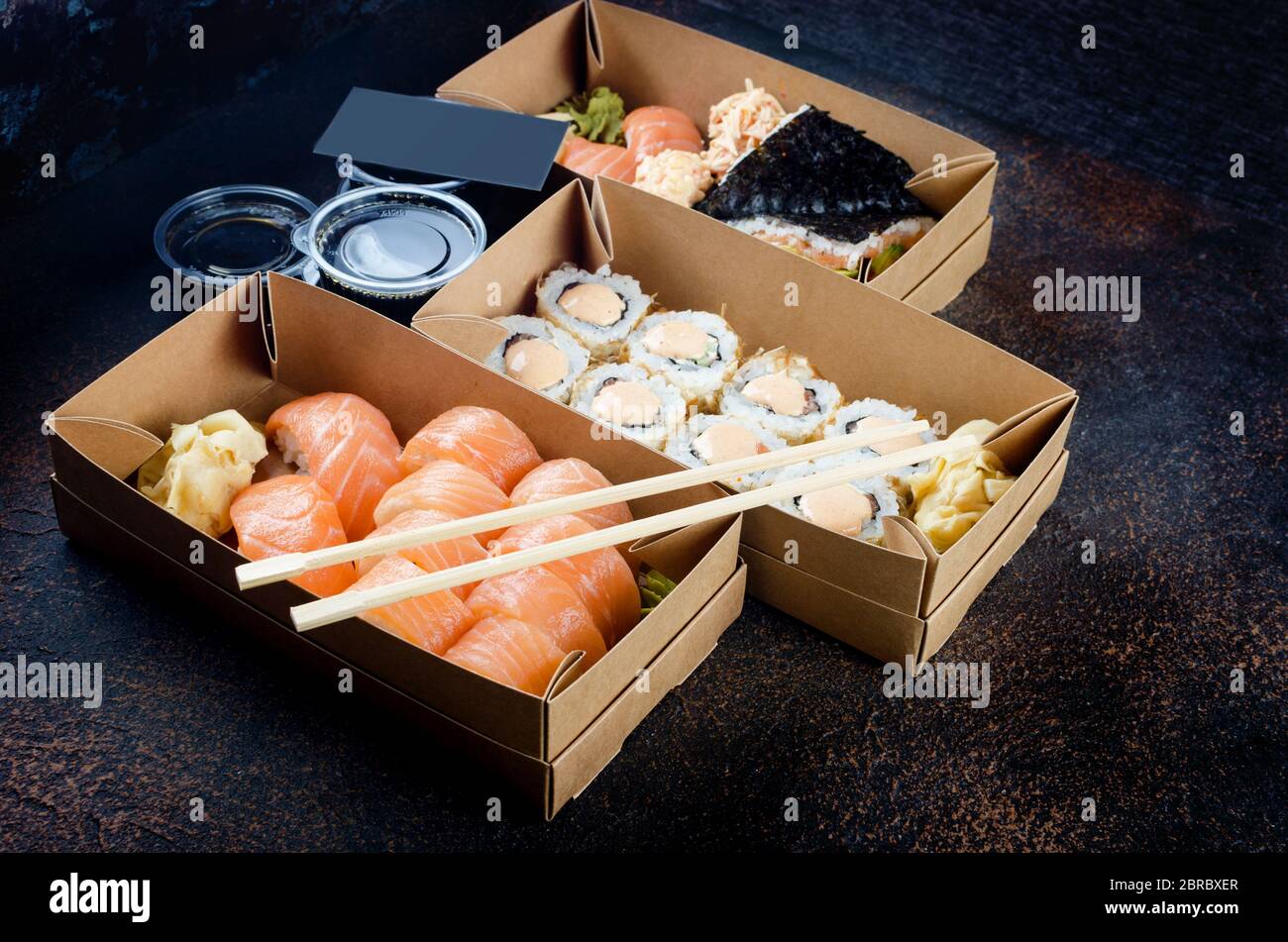 Leckere Sushi-Brötchen in Einweg-Kraftpapier-Boxen, Saucen, Essstäbchen. Sushi zum Mitnehmen oder Anliefern Stockfoto