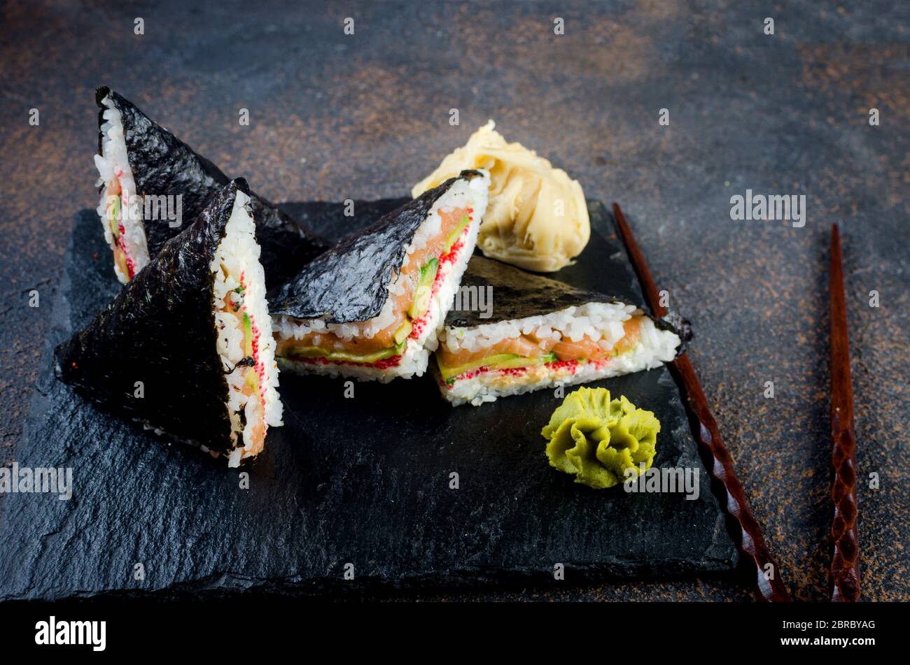 Leckere Sushi-Sandwiches mit Lachs auf schwarzem Steinteller mit Sojasoße, Ingwer, Wasabi Stockfoto