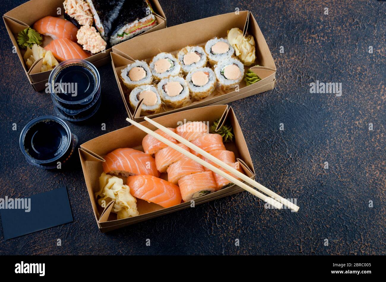 Leckere Sushi-Brötchen in Einweg-Kraftpapier-Boxen, Saucen, Essstäbchen. Sushi zum Mitnehmen oder Anliefern Stockfoto