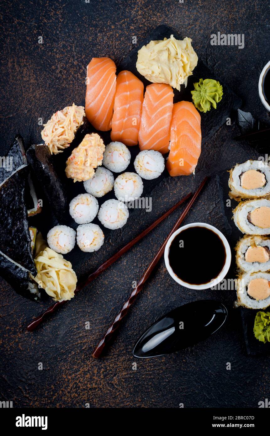 Leckere Sushi-Brötchen mit Soßen, Ingwer und Wasabi auf dunkel Stockfoto