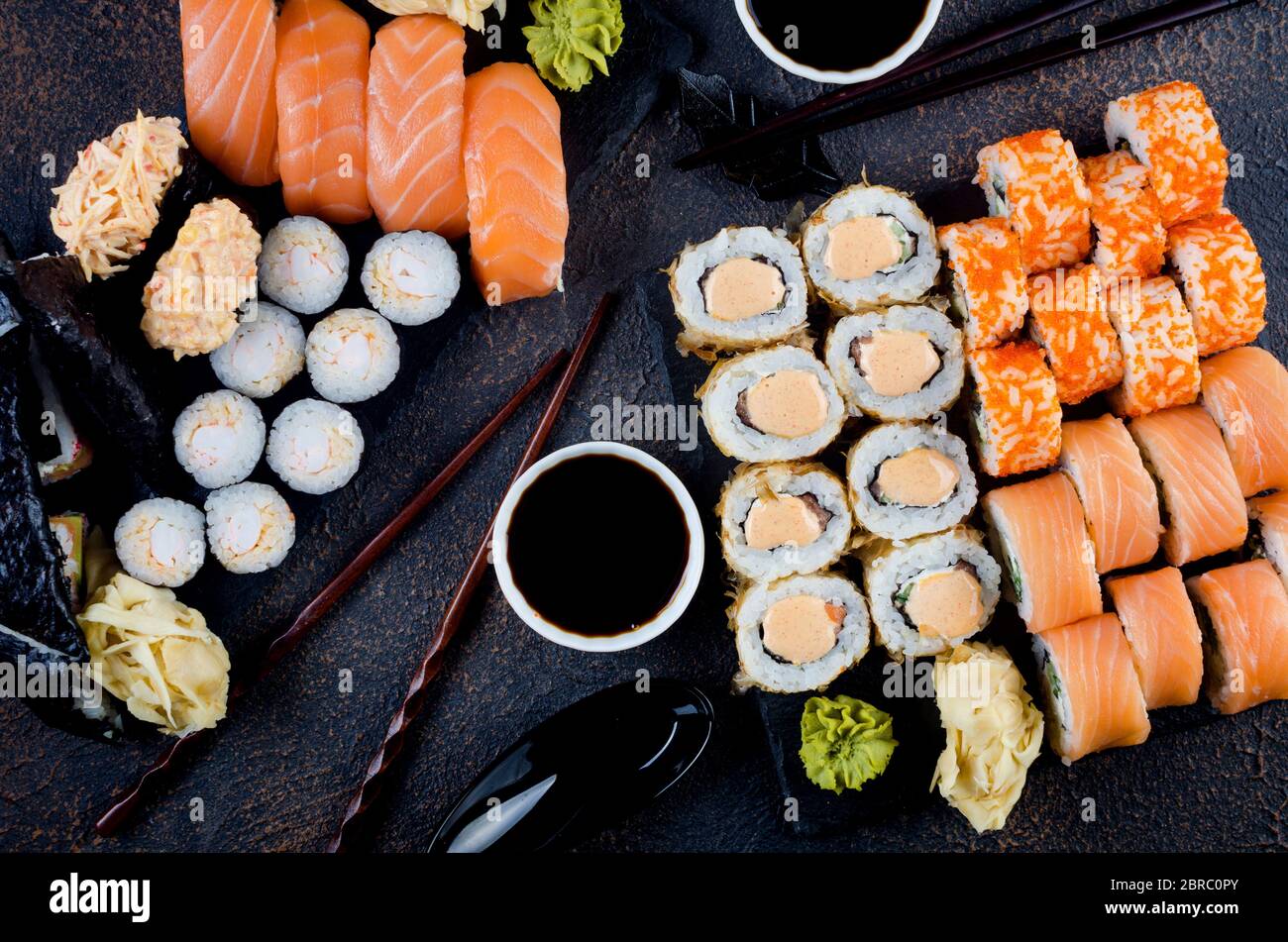 Leckere Sushi-Brötchen mit Soßen, Ingwer und Wasabi auf dunkel Stockfoto