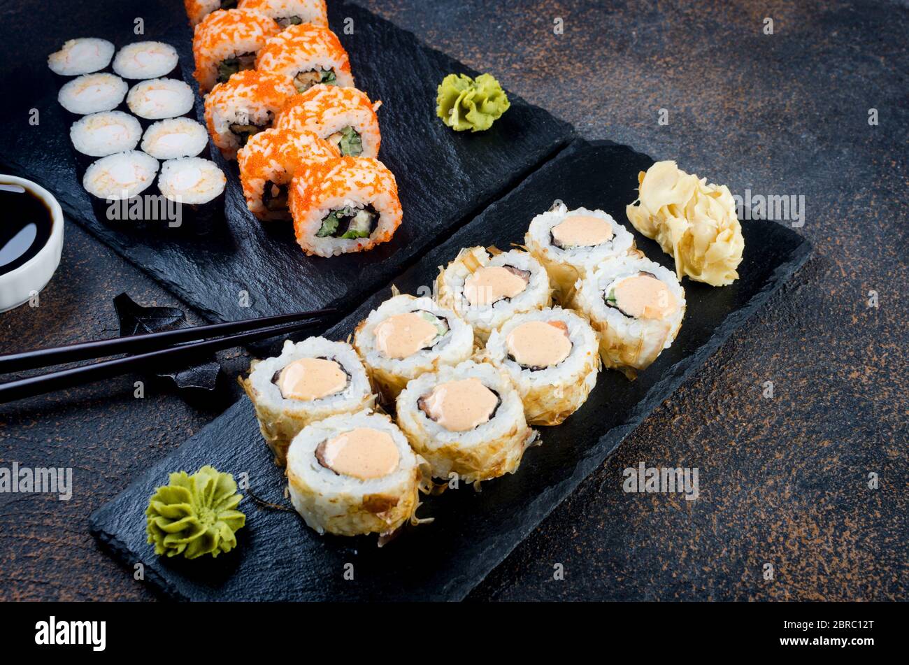 Maki-Brötchen auf Steinplatte mit Soßen, Ingwer und Wasabi Stockfoto