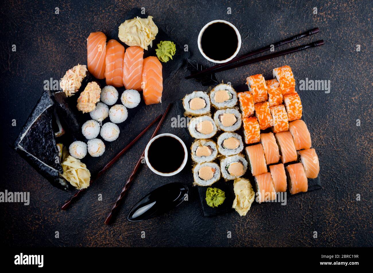 Leckere Sushi-Brötchen mit Soßen, Ingwer und Wasabi auf dunkel Stockfoto
