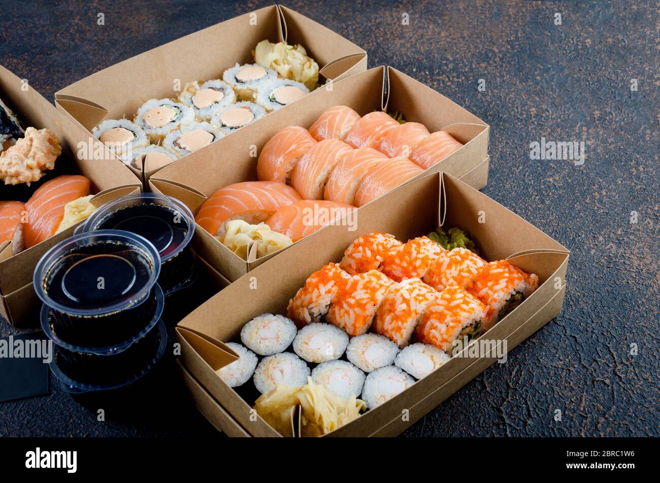 Leckere Sushi-Brötchen in Einweg-Kraftpapier-Boxen, Saucen, Essstäbchen. Sushi zum Mitnehmen oder Anliefern Stockfoto