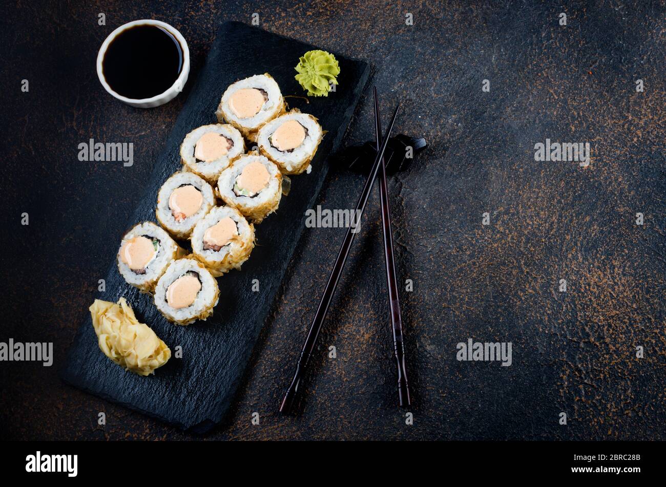 Sushi-Brötchen auf Steinplatte mit Saucen, Essstäbchen, Ingwer und Wasabi Stockfoto
