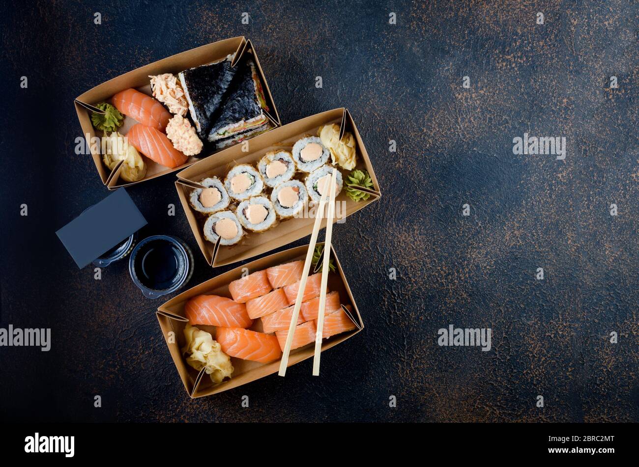 Leckere Sushi-Brötchen in Einweg-Kraftpapier-Boxen, Saucen, Essstäbchen. Sushi zum Mitnehmen oder Anliefern Stockfoto