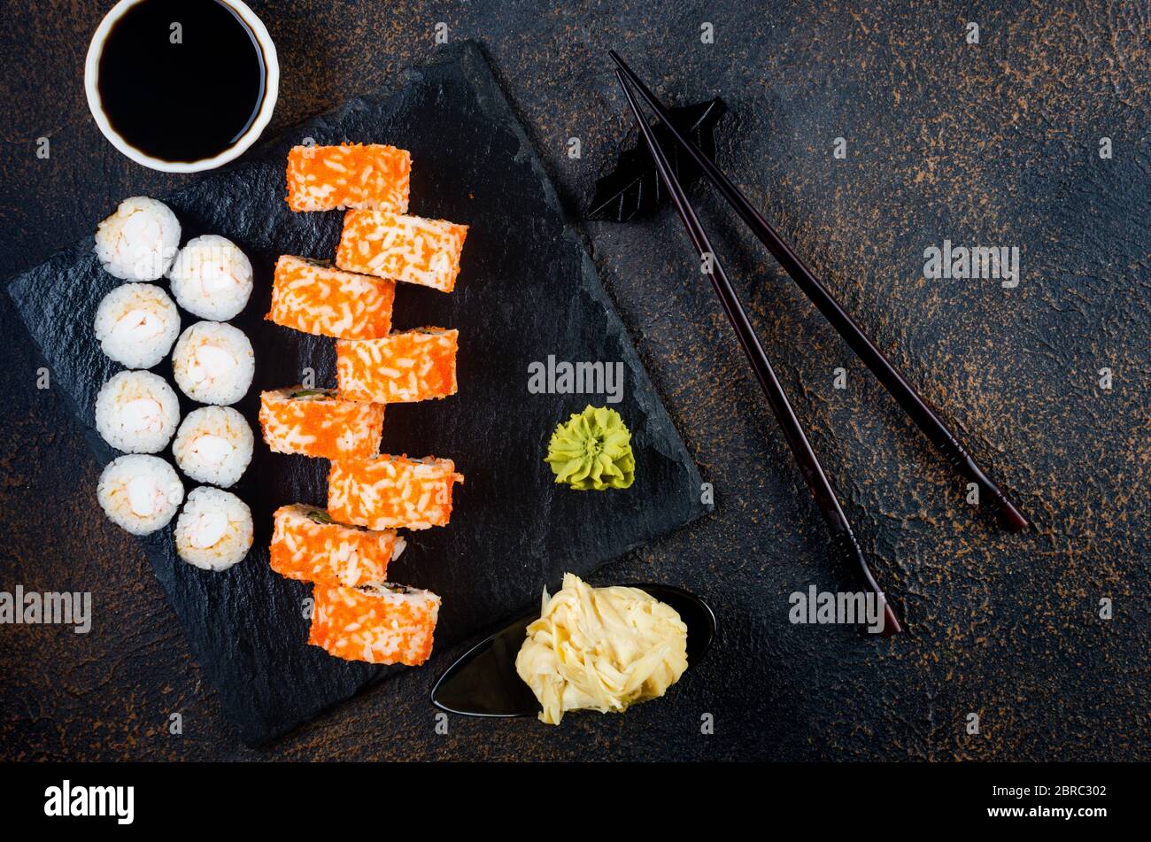 Maki-Brötchen auf Steinplatte mit Soßen, Ingwer und Wasabi Stockfoto