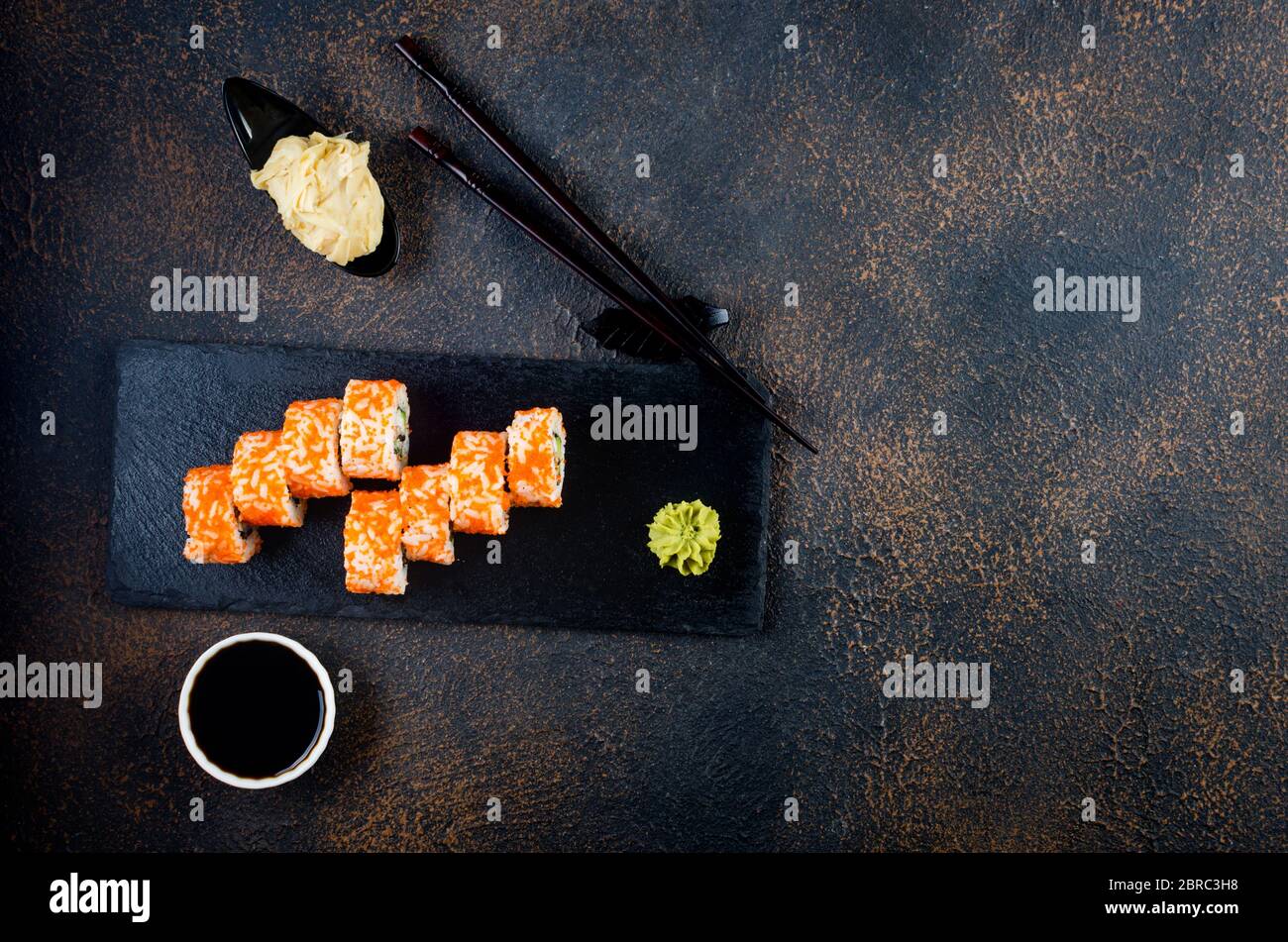 Sushi-Brötchen auf Steinplatte mit Saucen, Essstäbchen, Ingwer und Wasabi Stockfoto