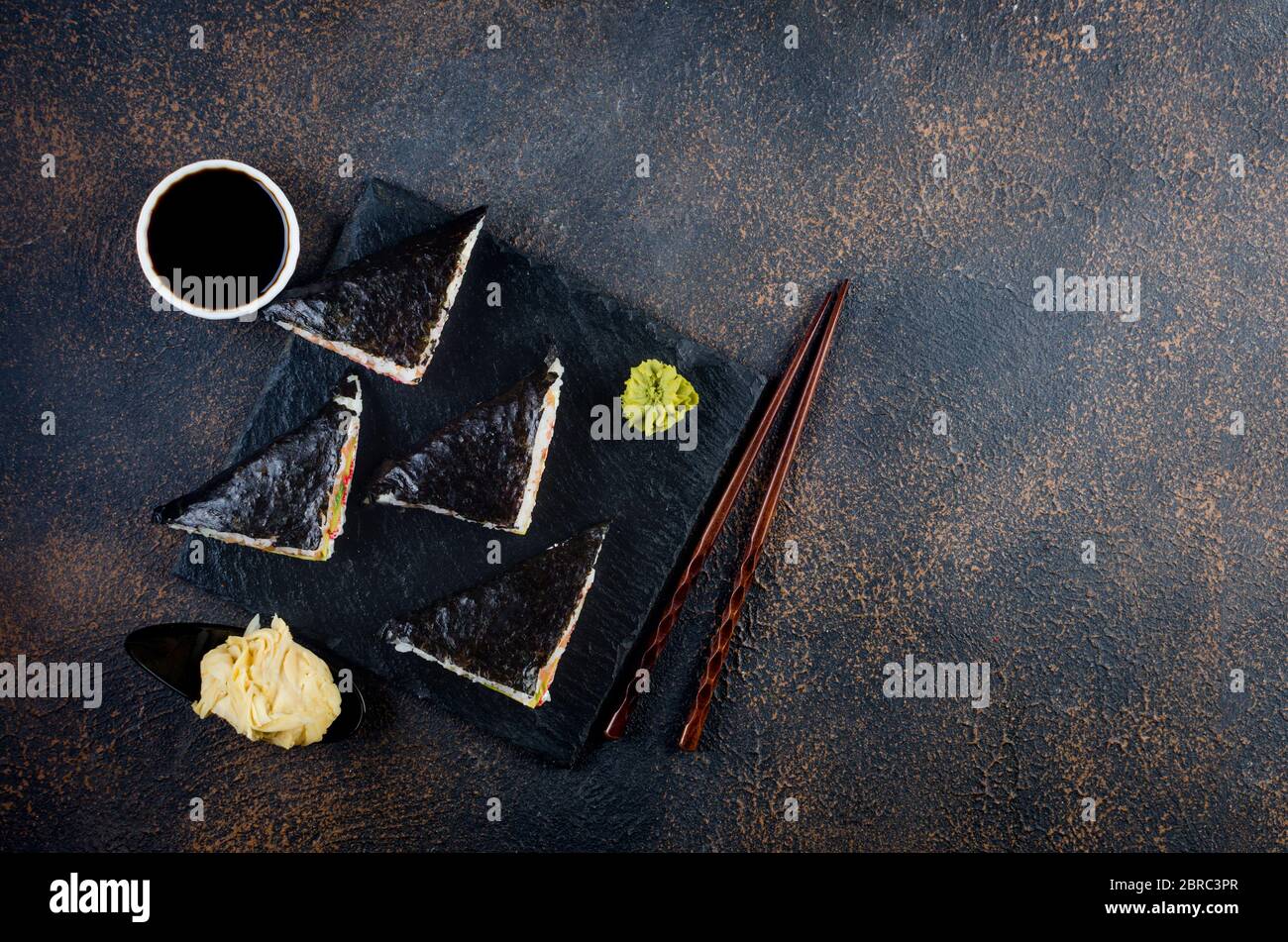 Leckere Sushi-Sandwiches mit Lachs auf schwarzem Steinteller mit Sojasoße, Ingwer, Wasabi Stockfoto