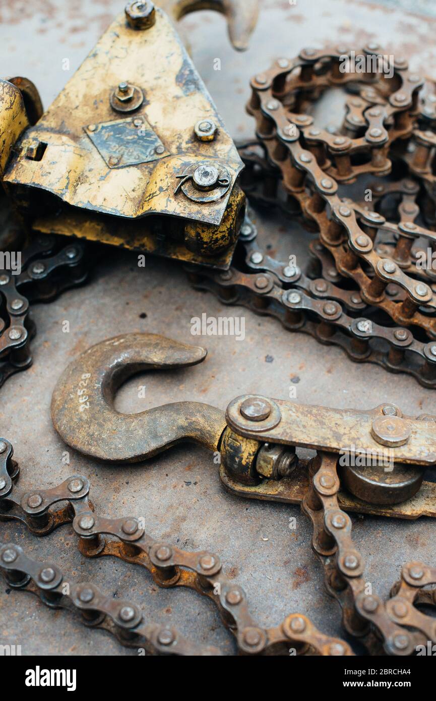 Alte rostige sowjetische selbstgemachte Winde, mit Spuren von gelber Farbe. Haken, Fahrradkette, Kettenglieder. Die Winde liegt auf einem Blech aus rostfreiem Eisen. Metallschrott. Stockfoto