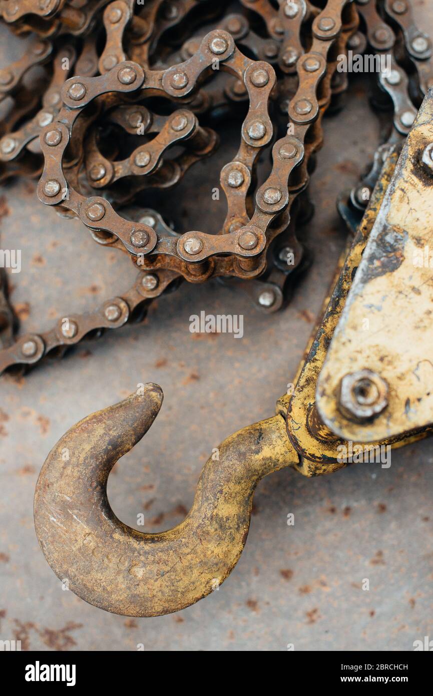 Alte rostige sowjetische selbstgemachte Winde, mit Spuren von gelber Farbe. Haken, Fahrradkette, Kettenglieder. Die Winde liegt auf einem Blech aus rostfreiem Eisen. Metallschrott. Stockfoto