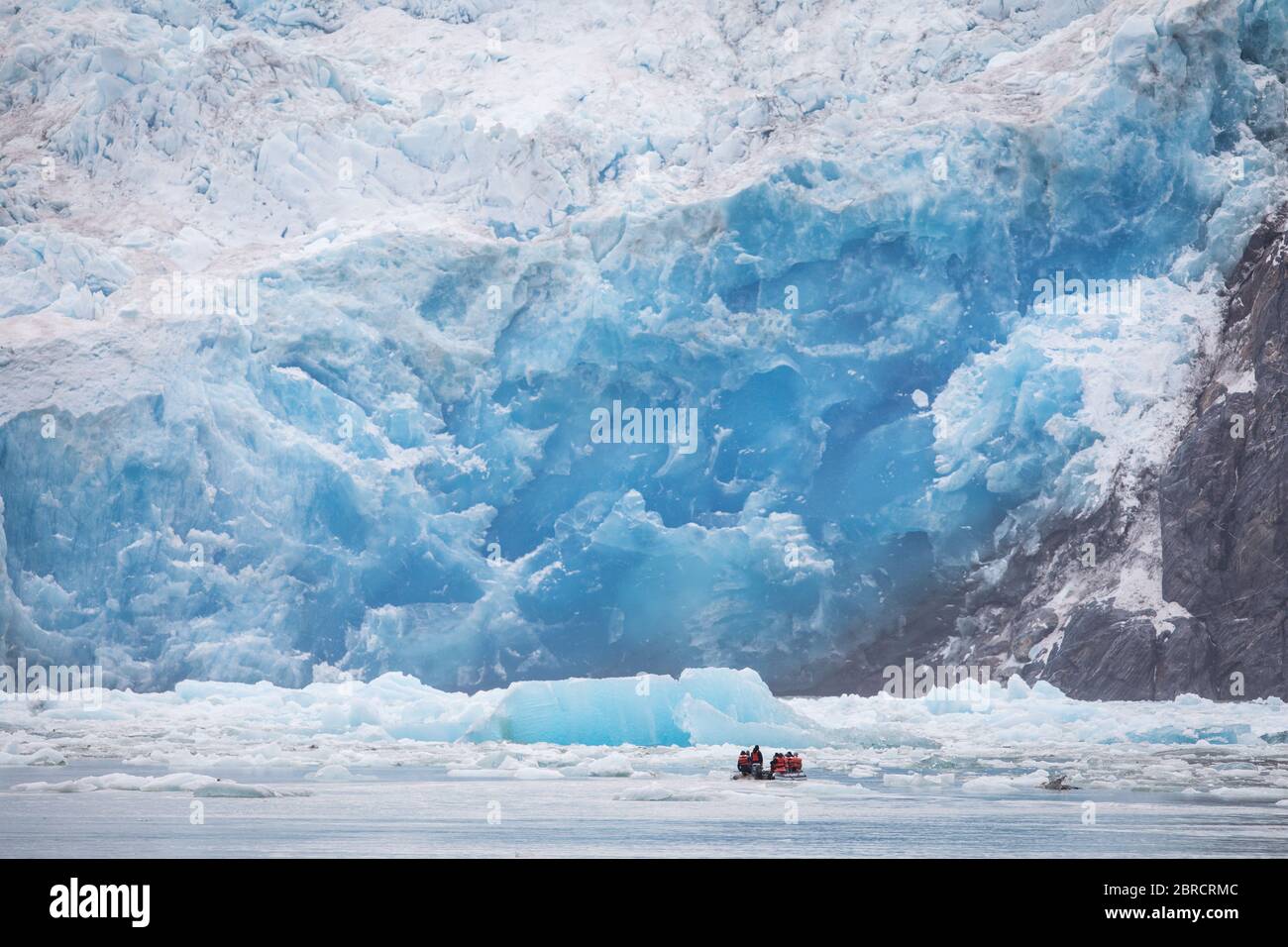 Touristen auf einem Skiff Boot erhalten eine aus der Nähe szenische Ansicht von Eisbergen Kalbskälte vom South Sawyer Glacier, schwimmend auf Tracy Arm Fjord, Südost-Alaska, USA Stockfoto