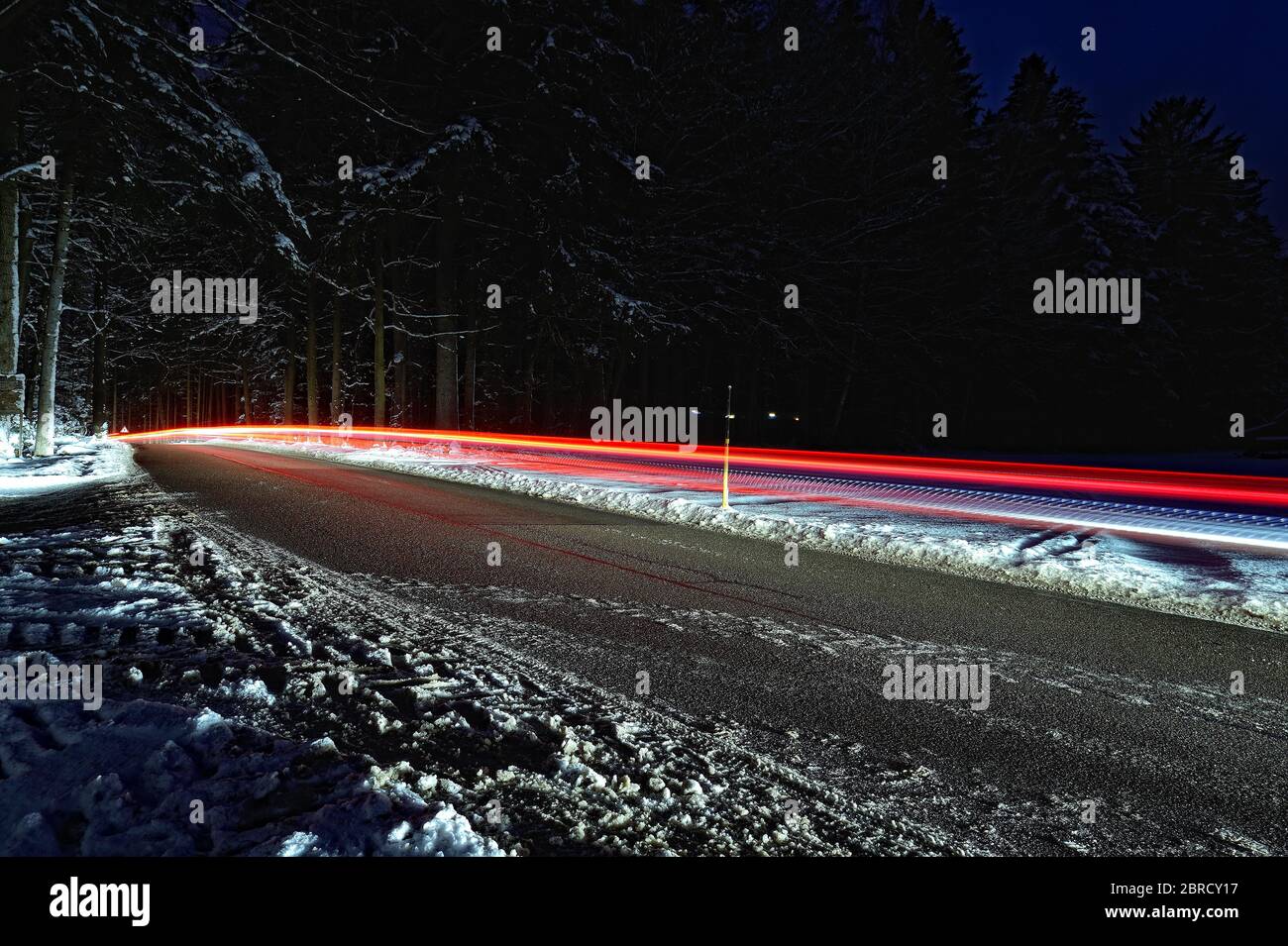 Verschneite Straße mit Rotlichtbahn bei Nacht, Deutschland Stockfoto