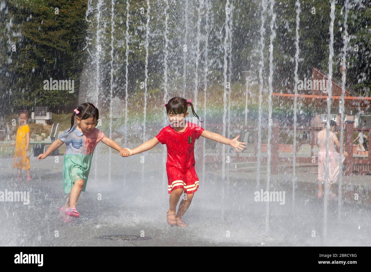 Mädchen, 4 und 6 Jahre, die durch Wasserstrahlen von einem Brunnen, Odongdo Island, Yeosu, Jeollanam-do, Südkorea laufen Stockfoto