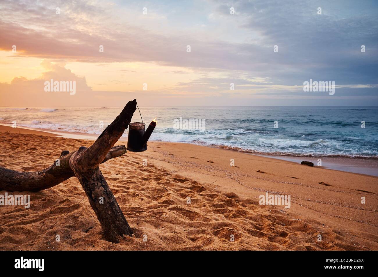 Tropischer Strand mit brennendem Kessel auf einem Holzbalken bei Sonnenaufgang, Sri Lanka. Stockfoto